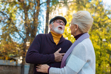 Fototapeta premium Caucasian senior man suffering, clutching and having chest pain cause from heart attack while walking in the park with his wife