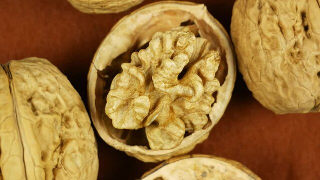 One opened walnut rotates near whole nuts on brown background