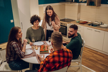 Fototapeta premium Group of friends enjoying dinner while sitting at the kitchen table together
