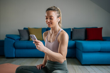 Naklejka na ściany i meble Woman using airpods and a smartphone while training at home