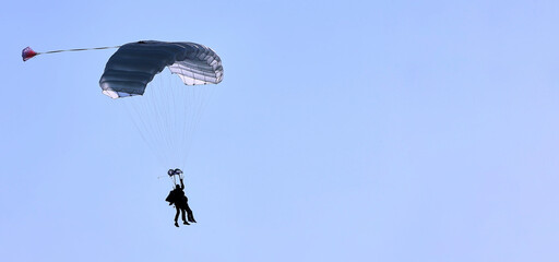 A skydiver with a white parachute canopy against a blue sky and white clouds, close-up.