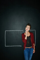 The best ideas are created outside the box. Studio shot of a thoughtful young woman posing with a chalk illustration of a box against a dark background.