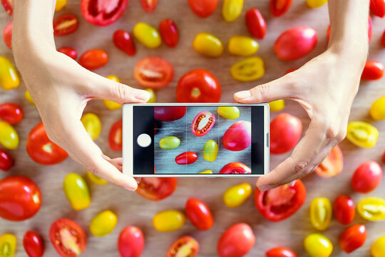 Close up of hands holding smartphone, taking photo of colorful vegetables on wooden table.