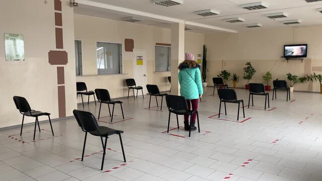 Concept of social distancing in waiting room at station. A woman enters an empty hall. One masked man is sitting on chair, keeping his distance. New normal life during pandemic.