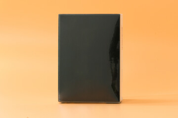 Vertical black box in plastic transparent wrapper on an orange background. Cardboard. Pack. Package. Blank. Container. Empty. Black. Box. Design. Product. Cardboard Box. Gift. Mock up. Mockup