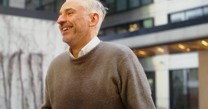 A gray-haired man laughs while talking to his interlocutor standing outdoors