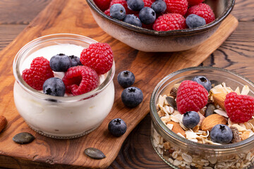 Healthy breakfast with yogurt and raspberries, blueberries, homemade muesli with nuts, on a wooden rustic table