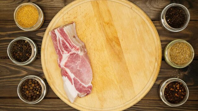 The cook prepares pieces of meat on a cutting board on a wooden table. A man's hand lays out a pork loin for marinating in the kitchen. Black peppercorns, clove, mustard, cumin, spices. Close-up