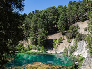 La Fuentona de Muriel en Soria, España, verano de 2021. Lago con aguas turquesas rodeado de árboles verdes y turistas disfrutando.