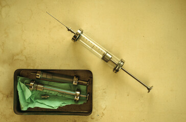 An old glass syringe with a needle on a yellowed sheet of paper. Vintage syringe.Problems of drug...
