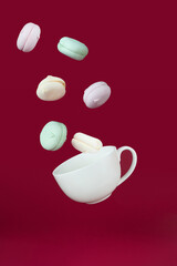 Fototapeta na wymiar concept of sweet dePorcelain cup flying with marshmallows on a red background. Morning and addiction concept.