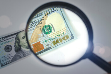 Zoom to money. Magnifying Glass - 100 US Dollars. Concept on the theme of checking money for authenticity.