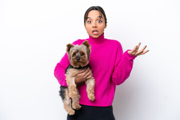 Young hispanic woman holding a dog isolated on white background with shocked facial expression