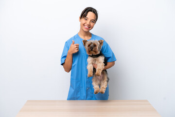 Young veterinarian woman with dog on a table isolated on white background with thumbs up because...