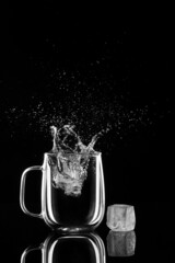 glass with water ice and splashes on a black background