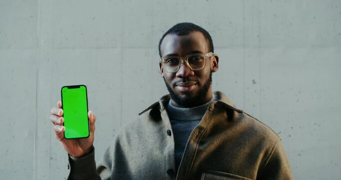 African american man looking at camera holding mobile phone with green screen