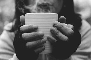 Mujer sosteniendo y soplando una taza de café caliente en blanco y negro
