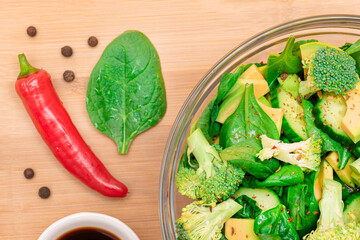 Fresh Green Salad of Avocado, Broccoli, Spinach and Cucumber with Soy Sauce and Red Hot Pepper on Wooden Cutting Board. Vegan Salad. Vegetarian Culture. Raw Food. Healthy Eating and Vegetable Diet