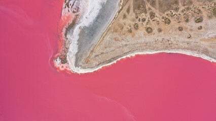 Flying over a pink salt lake. Salt production facilities saline evaporation pond fields in the salty lake. Dunaliella salina impart a red, pink water in mineral lake with dry cristallized salty coast