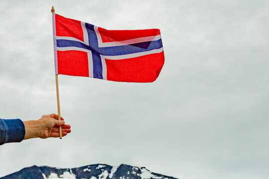 Hand Holds Norwegian Flag Against Mountain Nature