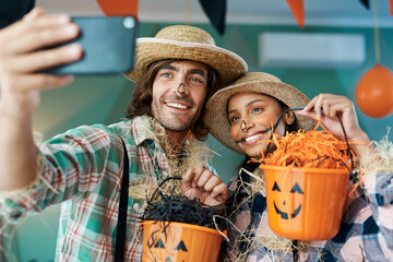 All treats, no tricks this year. Shot of a young couple taking selfies while holding buckets at...