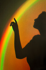 Shadow of woman. Rainbow reflection of sunbeam on wall. Hand touches rainbow beam. Concept of dreams and hopes.
