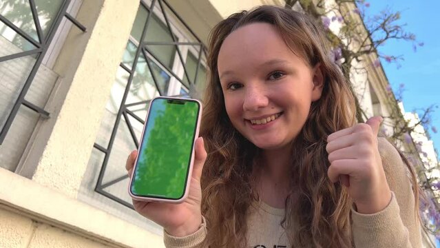 Teenager girl very cute smiles in the frame shows the screen of the phone and turns the pages swaying on the screen and class. High quality 4k footage