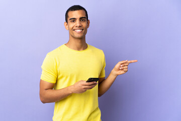 African American man over isolated purple background using mobile phone pointing finger to the side