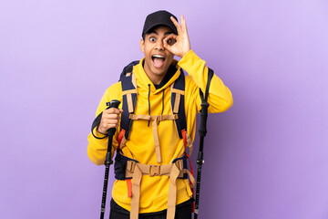 African American man with backpack and trekking poles over isolated background showing ok sign with fingers