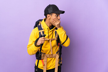 African American man with backpack and trekking poles over isolated background covering mouth and looking to the side