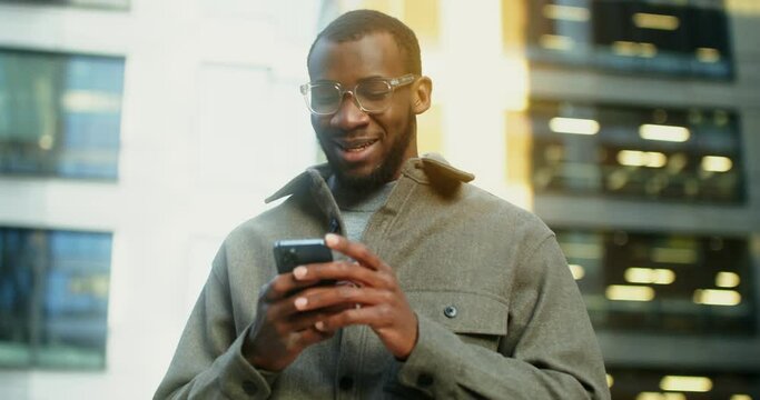 African-American man uses a mobile phone standing near a building in Evening
