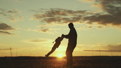 Fototapeta na wymiar Father circles hands of his beloved baby in sun on field, baby laughs in flight. Dad, child, daughter are playing in park at sunset. Healthy family and childhood. Happy family. Child have fun in