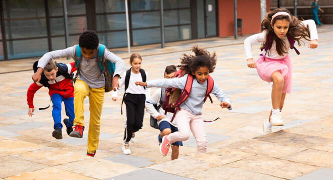 Portrait of cheerful tween boys and girls with school backpacks running in schoolyard in spring day.