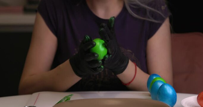 The girl paints Easter eggs with her hands in black gloves.