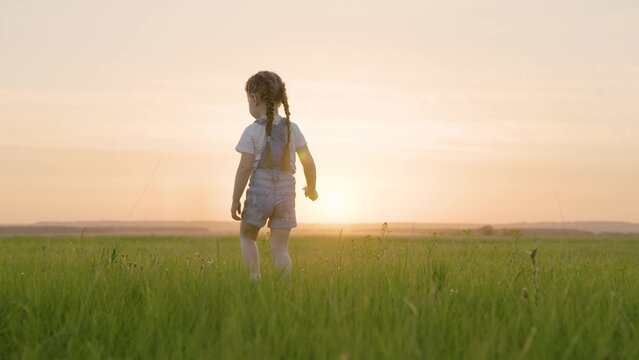 Happy child, girl walks on green grass in spring park. Kid walks outdoors in summer. Healthy outdoor games for children. A childhood dream. Happy family, childhood. Child having fun in the meadow