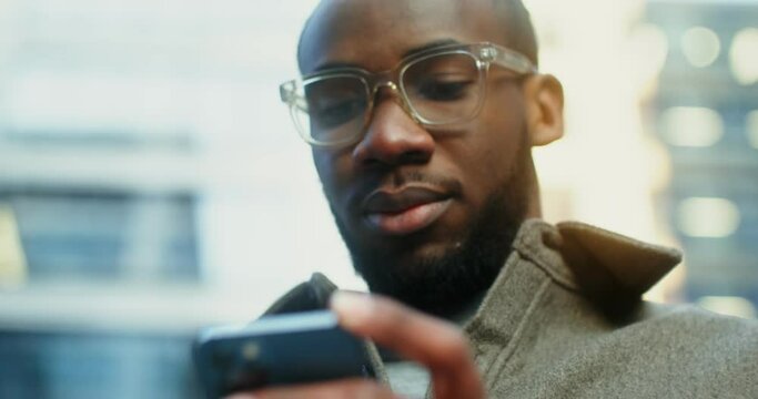 African-American man uses a mobile phone standing near a building in Evening