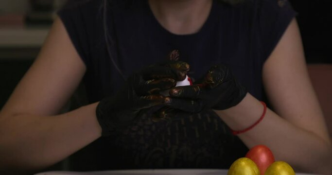 The girl paints Easter eggs with her hands in black gloves.