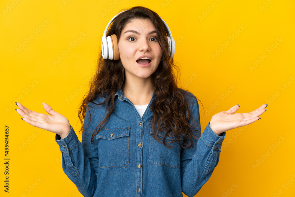 Wall mural Teenager Russian girl isolated on yellow background surprised and listening music