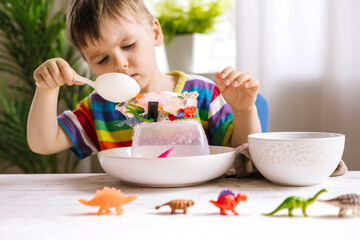 A cute little child pours warm water over toys frozen in ice. Dinosaur defrosting. Early development