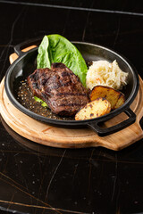 Grilled steak with baked golden potatoes served with sour cabbage and red sauce on a dark background. Delicious Recipe. Pork Fillet Cooked on Skillet for Dinner . Fried Juicy Meat Texture.
