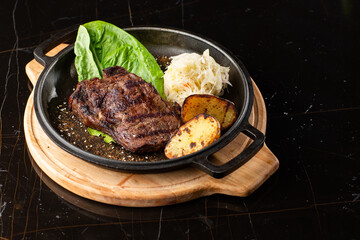 Grilled steak with baked golden potatoes served with sour cabbage and red sauce on a dark background. Delicious Recipe. Pork Fillet Cooked on Skillet for Dinner . Fried Juicy Meat Texture.