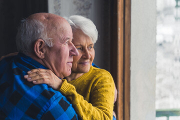 satisfied senior couple embracing and looking children in the garden from the window senior people support concept medium closeup indoors. High quality photo