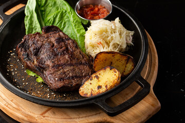 Grilled steak with baked golden potatoes served with sour cabbage and red sauce on a dark background. Delicious Recipe. Pork Fillet Cooked on Skillet for Dinner . Fried Juicy Meat Texture.