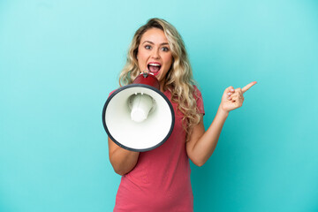 Young Brazilian woman isolated on blue background shouting through a megaphone and pointing side