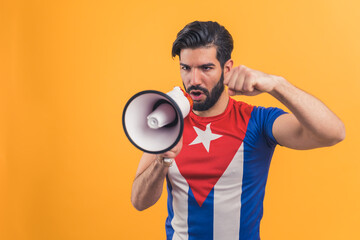 Young caucasian bearded attractive active leader happy man 20s wearing Cuban flag t-shirt speaking in loudspeaker isolated on yellow background studio portrait. High quality photo
