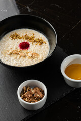 Obraz na płótnie Canvas Semolina porridge for breakfast oat with nuts in black bowl served with honey isolated on black stone background. Homemade food. Tasty breakfast. Selective focus.