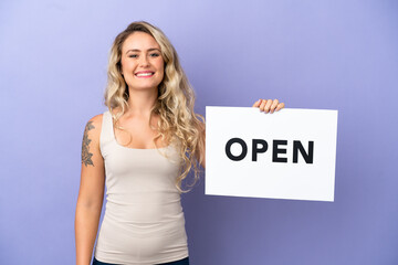 Young Brazilian woman isolated on purple background holding a placard with text OPEN with happy expression