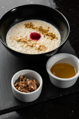 Semolina porridge for breakfast oat with nuts in black bowl served with honey isolated on black stone background. Homemade food. Tasty breakfast. Selective focus.
