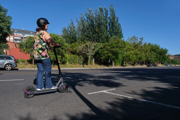 Latin mature woman with a helmet riding her electric kick scooter; road safety