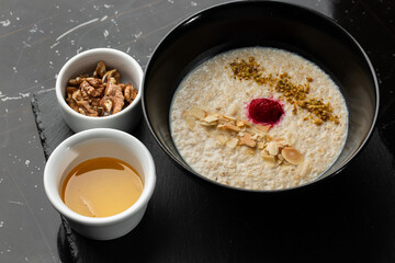 Semolina porridge for breakfast oat with nuts in black bowl served with honey isolated on black stone background. Homemade food. Tasty breakfast. Selective focus.